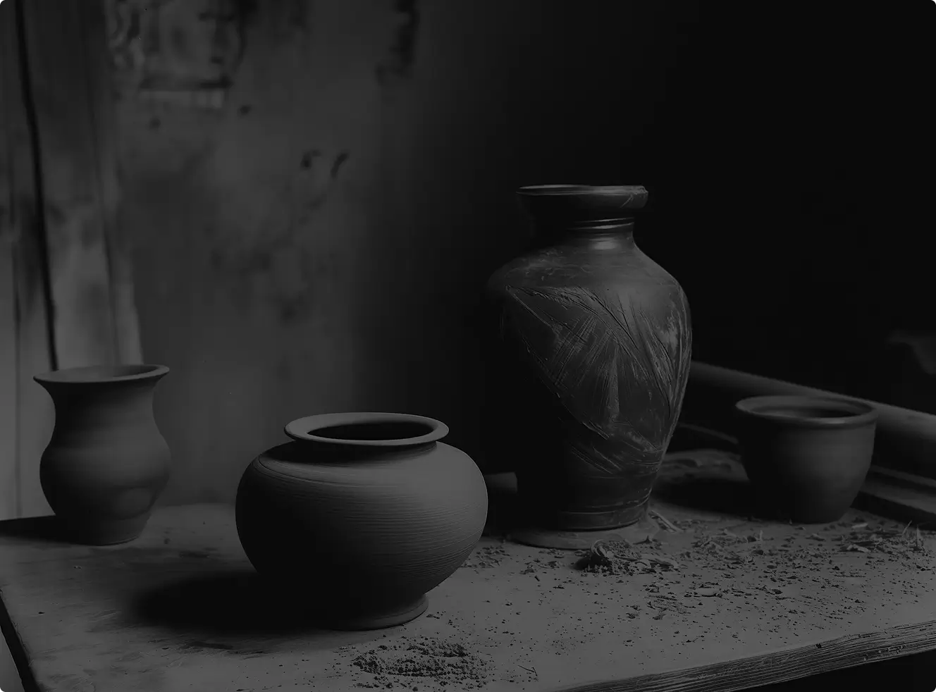 Four handcrafted clay pots of different shapes placed on a wooden surface with scattered clay dust.
